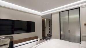 A modern hotel room with a bed, a desk, a chair, a TV, and a wardrobe.