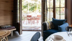 A room with a wooden floor, a sofa with a blue cushion, a bench with a plaid blanket, a wicker chair, and a table with a bowl and glass. - Holiday Home in Name - Namur (Gedinne)