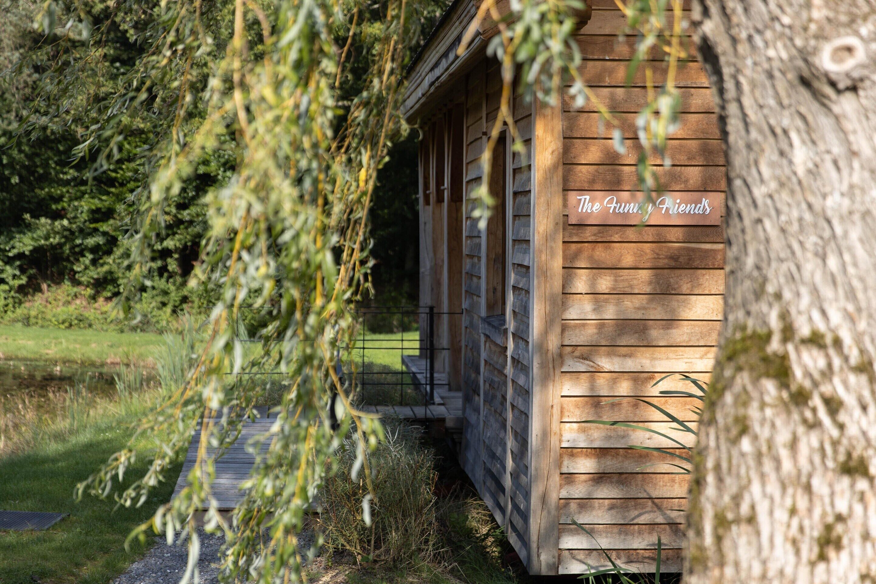 A wooden cabin with a sign reading "The Funky Friends" in a natural setting with trees and a pathway.