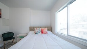 Un dormitorio con cama, ventana, silla y escritorio.