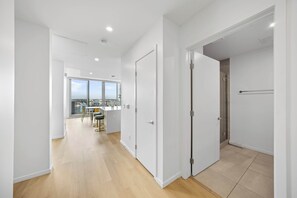 Een modern appartement met een houten vloer, witte muren en uitzicht op de stad door grote ramen.