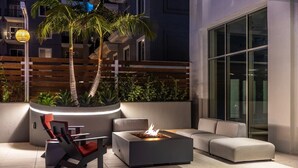 An outdoor seating area with a fire feature, modern furniture, and a palm tree. - @marbella Lane - 3BR Coastal Retreat w/ Luxe Touch (Long Beach)