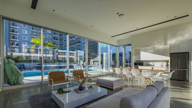 Un salon moderne doté d’une grande baie vitrée, offrant une vue sur la piscine, et comprenant un espace cuisine.