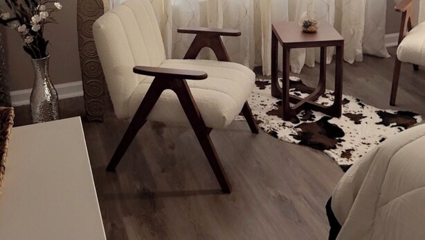 Un salón con un sillón blanco, una mesita de madera y un jarrón decorativo con flores secas.
