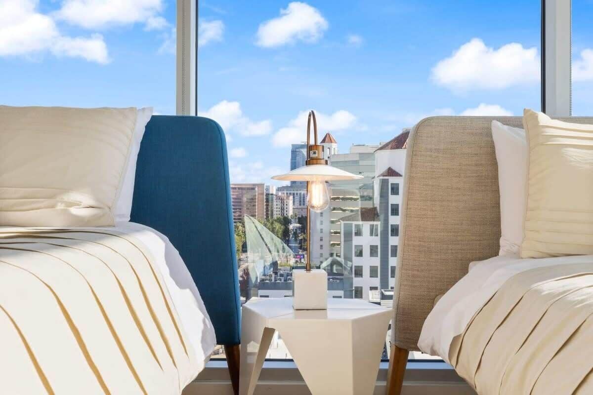 Et hotelværelse med to senge, et lille bord og udsigt over byen gennem store vinduer.