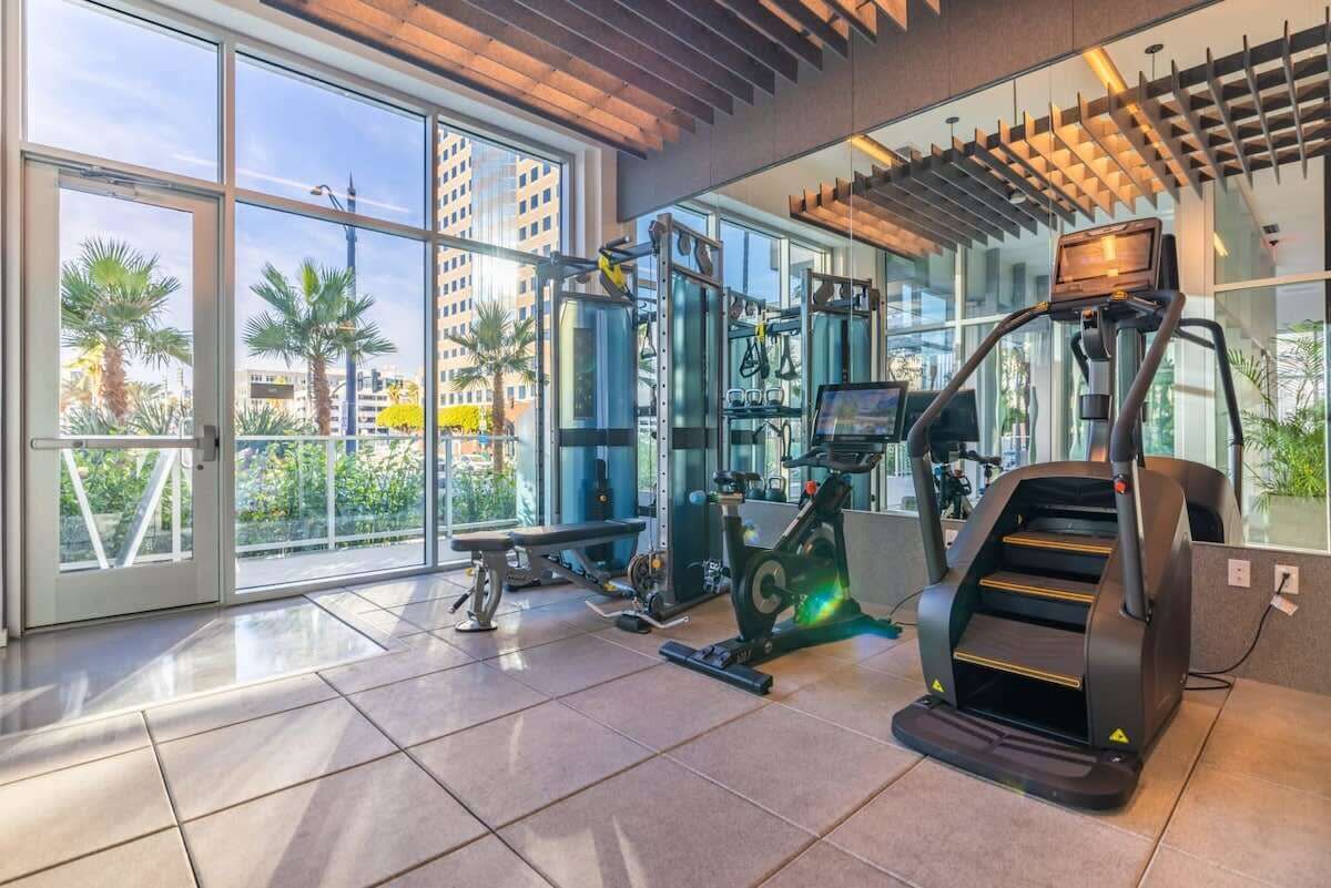 A modern gym with exercise equipment, large windows, and a view of palm trees.