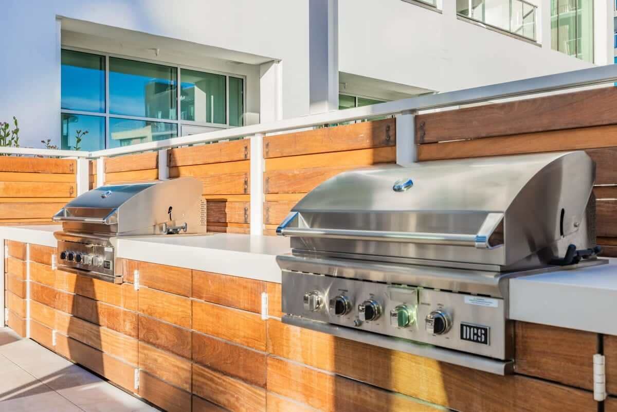 Une cuisine extérieure équipée de deux barbecues, d’un évier encastré et d’un pare-feu en bois.