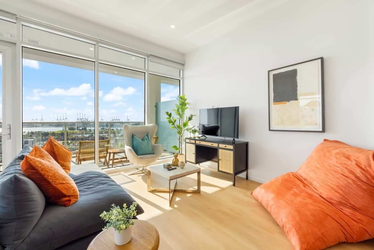 A modern living room with a sofa, coffee table, and TV, large windows with a city view, and a plant on the coffee table.