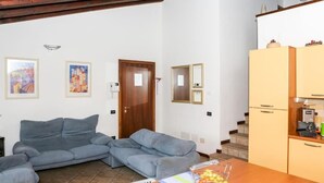 Una sala de estar con un sofá gris, una mesa de madera con fruta, y una cocina con armarios y electrodomésticos.