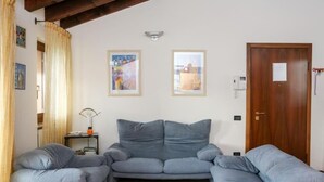 Una habitación con un sofá gris, una puerta de madera y dos cuadros en la pared.