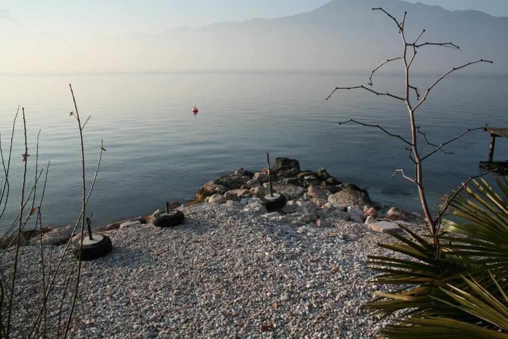 Una spiaggia con ciottoli, un promontorio roccioso e un lago calmo.