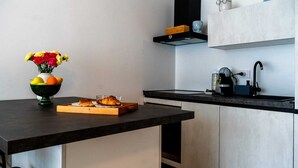 Una cocina moderna con encimera negra, un jarrón de flores, un bol de fruta y un croissant sobre una tabla de madera.