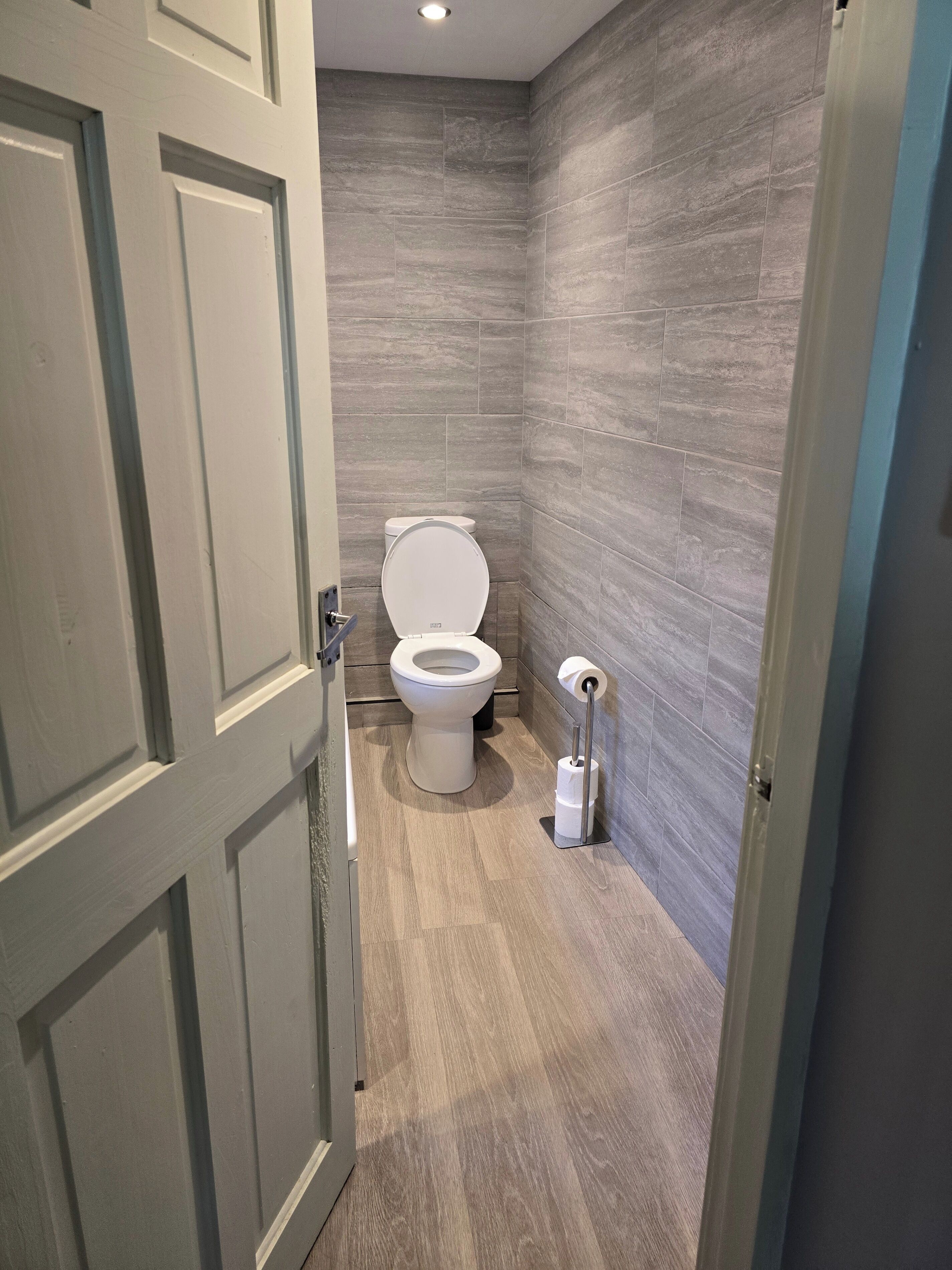 Um banheiro moderno com vaso sanitário, suporte para papel higiênico e piso de madeira.