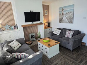 A modern living room with a grey sofa, a wooden coffee table, and a television mounted on the wall. - Eden Rose Cottage in Morecambe hot tub (Morecambe)