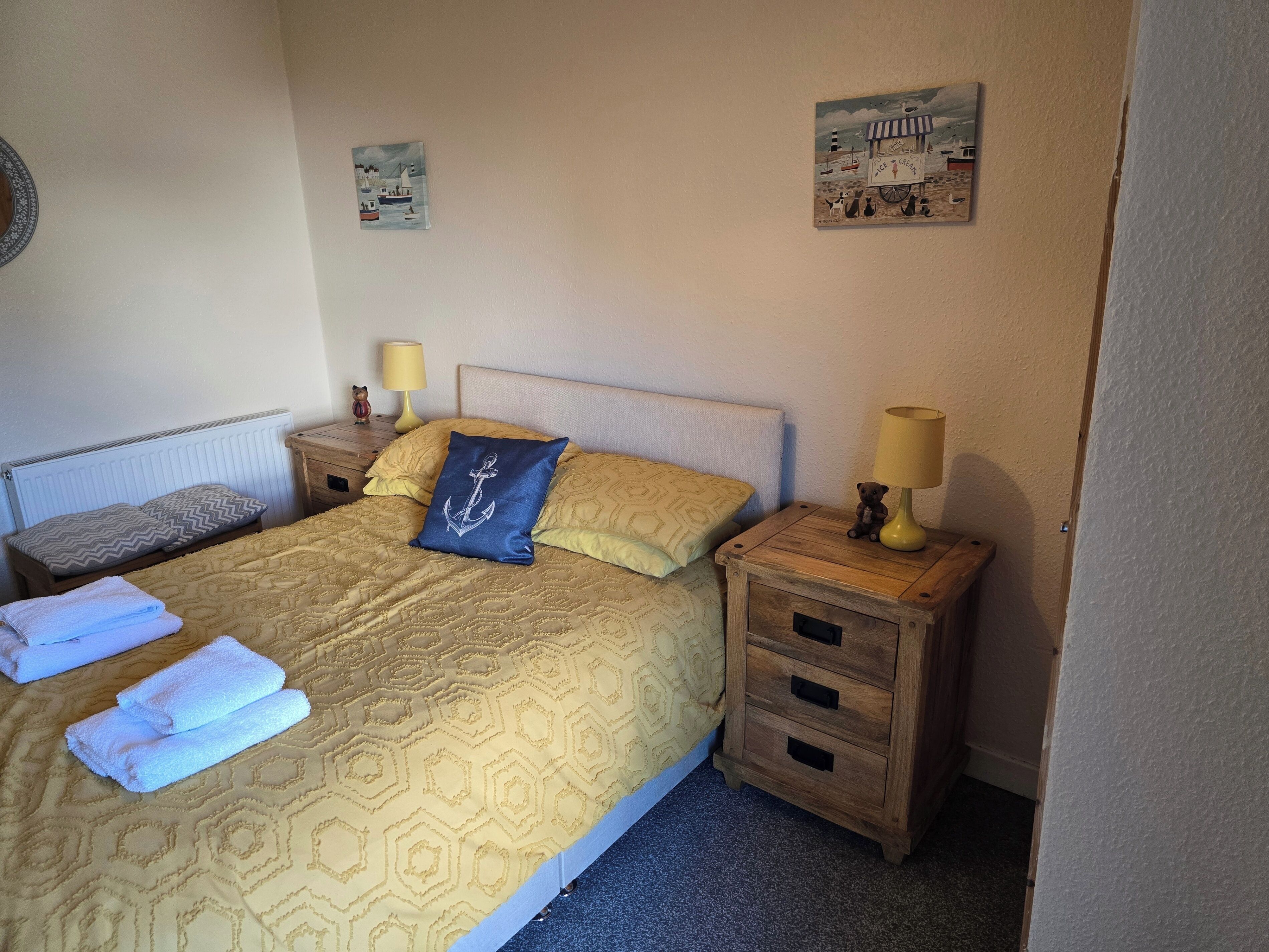 A neatly made bed with a patterned bedspread, two pillows, and a set of towels. There are two bedside tables with lamps and a small figurine on one.