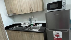Una cocina compacta con armarios de madera, un refrigerador de acero inoxidable, un microondas y un lavamanos.