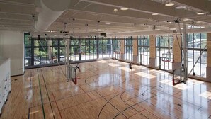 An indoor basketball court with a wooden floor, large windows, and ceiling-mounted equipment. - Modern Luxury | DC | Free Parking (Arlington)