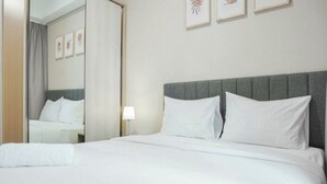 A hotel room with a large bed, a grey headboard, white bedding, a bedside lamp, and framed artwork on the wall. - Cozy Clean Nice Puri Mansion Apartment (Jakarta)
