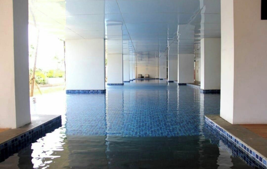 Uma grande piscina interior com água azul cristalina, rodeada por paredes e colunas brancas.