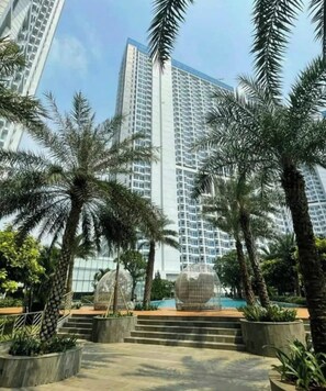 A high-rise building with a modern design, surrounded by palm trees and a glass structure. - Cozy Clean Nice Puri Mansion Apartment (Jakarta)