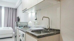 A compact hotel kitchen with a sink, a dish rack, a washing machine, and a flat-screen TV. - Cozy Clean Nice Puri Mansion Apartment (Jakarta)