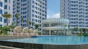 A modern building with a glass facade, surrounded by a swimming pool and palm trees. - Cozy Clean Nice Puri Mansion Apartment (Jakarta)