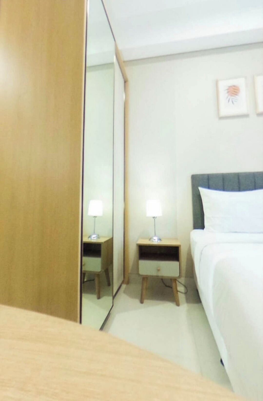 A hotel room with a bed, two bedside tables with lamps, a mirror, and a wall-mounted picture.