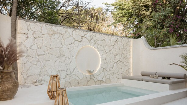 A spa area with a stone wall, a hot tub, and a seating area with cushions. - Aesthetic Design Suite Aire with Pool (Cancún)