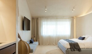 Una camera da letto moderna con un letto, una televisione, un'ampia finestra con tende e un tappeto rotondo.