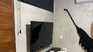 A modern living room with a flat-screen TV mounted on the wall, a wooden bench, a white chair, and a black umbrella hanging on the wall. - #NEW*Down Town Loft pool in the heart of Cancun (Cancún)