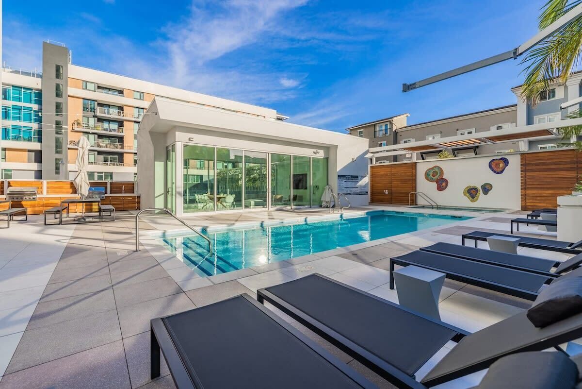 Zona de piscina d'un hotel modern, amb gandules, una piscina tancada amb vidre i vista als edificis circumdants.