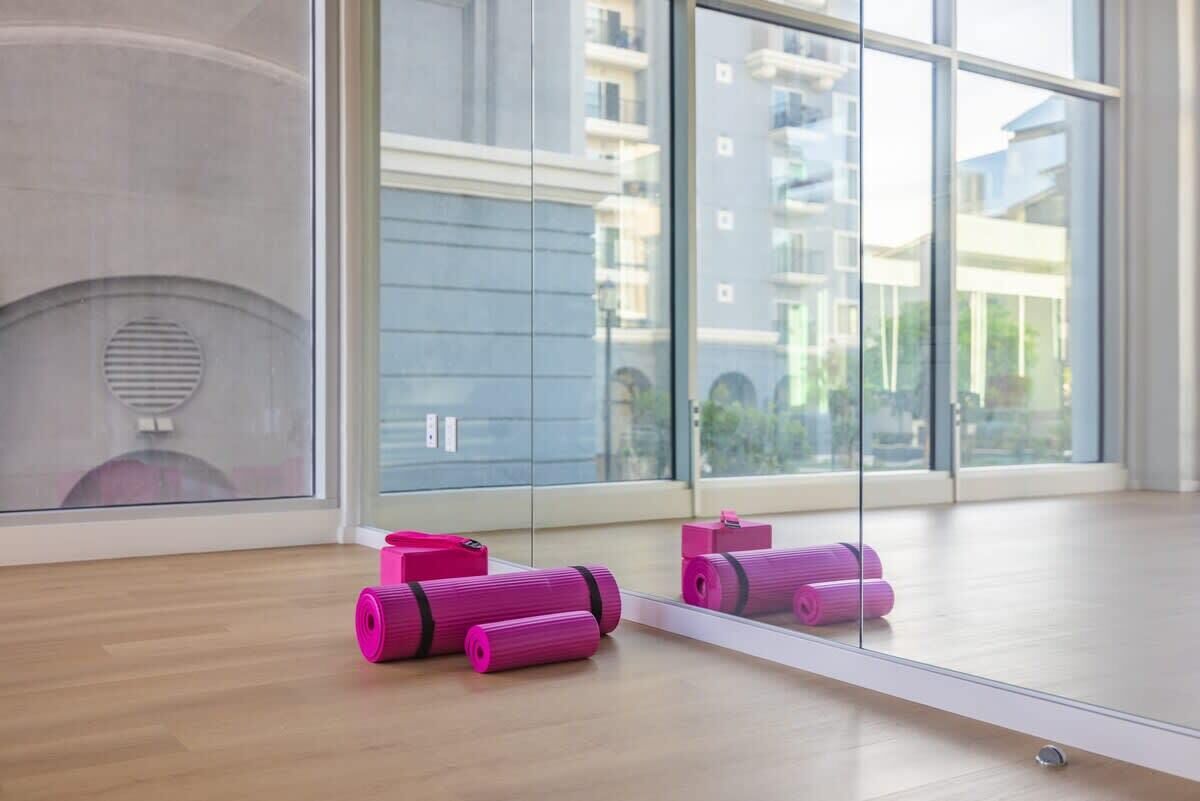 Una habitación con amplios ventanales, suelo de madera y colchonetas de yoga color rosa.
