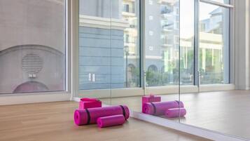 Una habitación con amplios ventanales, suelo de madera y colchonetas de yoga color rosa.