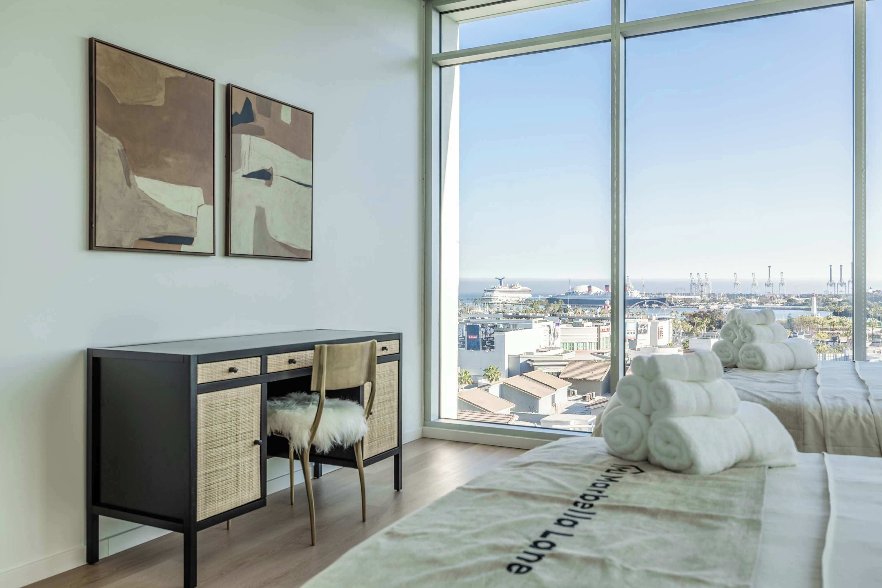Une chambre d'hôtel moderne dotée d'une grande fenêtre, d'un bureau avec des paniers en osier et d'un lit avec des serviettes.