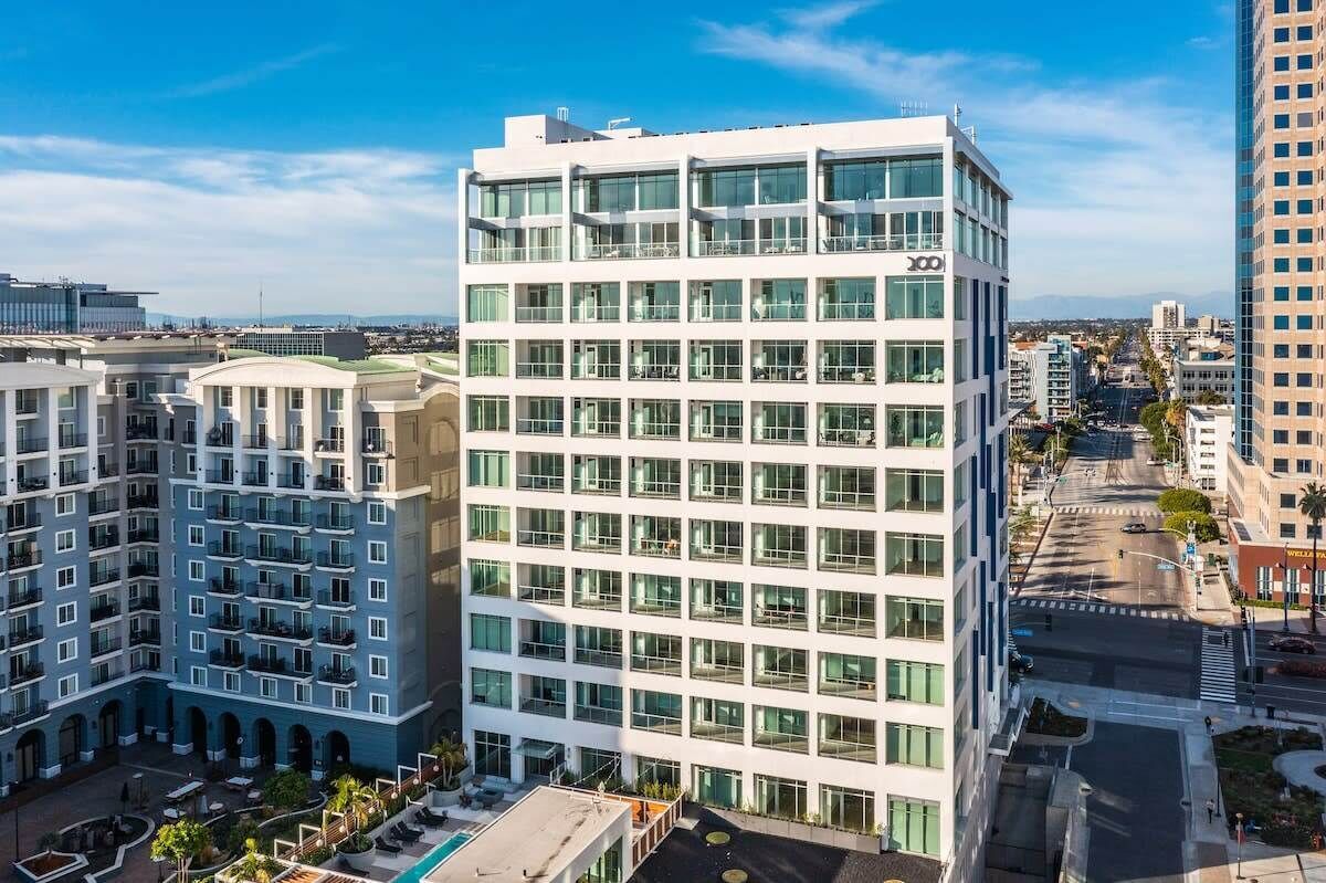 A modern multi-story hotel with a glass facade, multiple balconies, and a rooftop pool area.