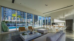 A modern living room with a large glass window, a pool view, and a kitchen area. - @ Marbella Lane - Panoramic Delight Dream Escape! (Long Beach)