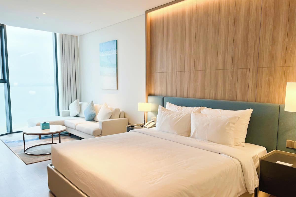 A hotel room with a large bed, a sofa, a coffee table, and a view of the outdoors.