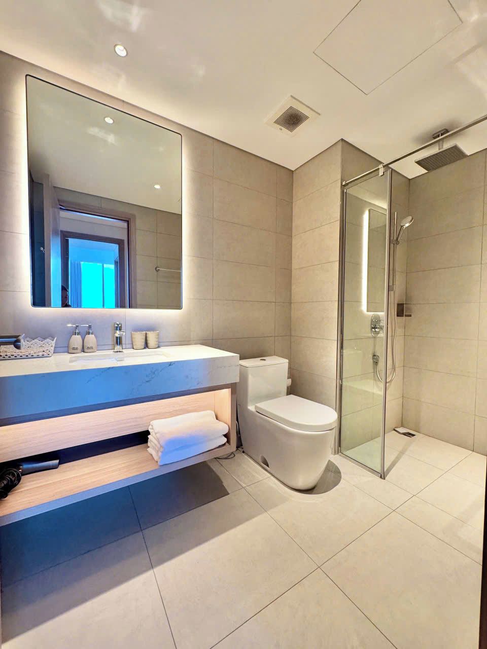 A modern bathroom with a large mirror, a toilet, a shower enclosure, and a vanity with a sink.