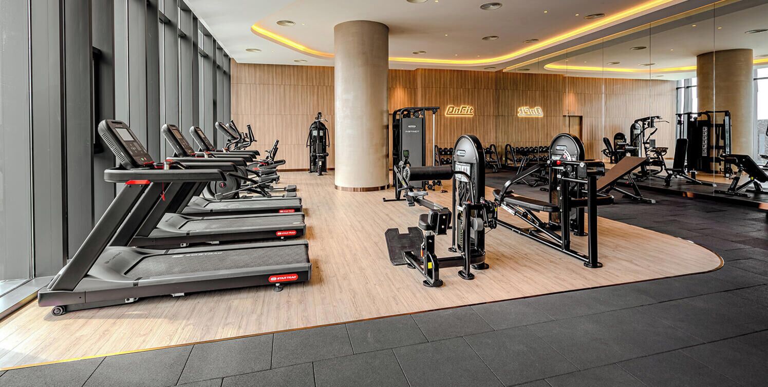 A modern gym with treadmills, weight machines, and a wooden floor.