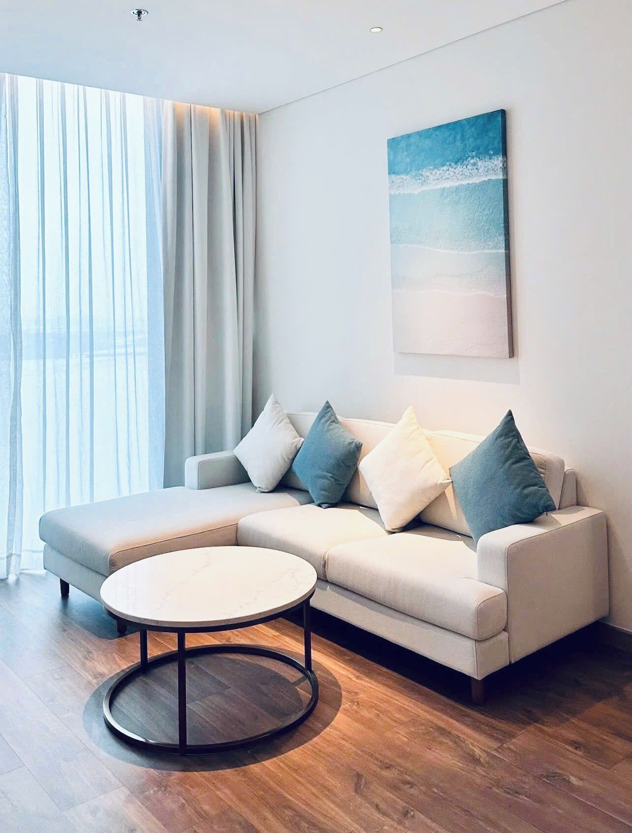 A modern living room with a sectional sofa, a round coffee table, and a large painting of a beach scene.