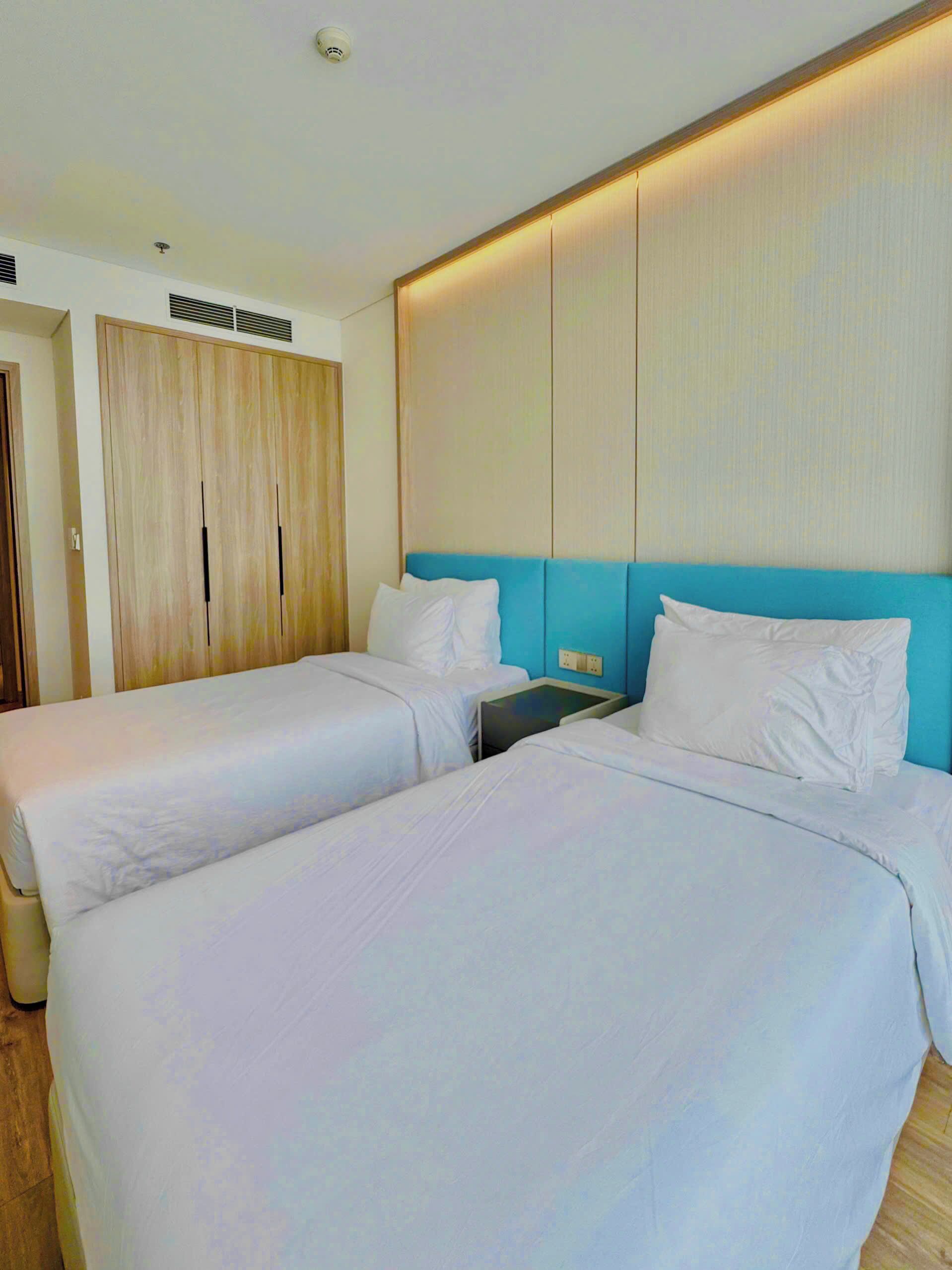 Une chambre d’hôtel avec deux lits, une armoire, une table de chevet et un luminaire fixé au mur.