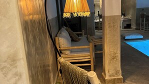 A lounge area with a wicker chair, a hanging lamp, and a pool in the background. - Charming, recently renovated riad in the medina of Marrakech (Marrakech)