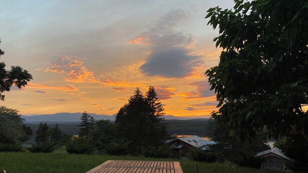 A wooden table and chairs in a grassy area with a view of mountains and a sunset. - An Apartment with a View: A peaceful getaway in Hudson, NY (Hudson)
