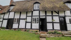 A traditional Tudor-style building with a thatched roof, black and white timber framing, and a small garden area with stepping stones leading to the entrance.