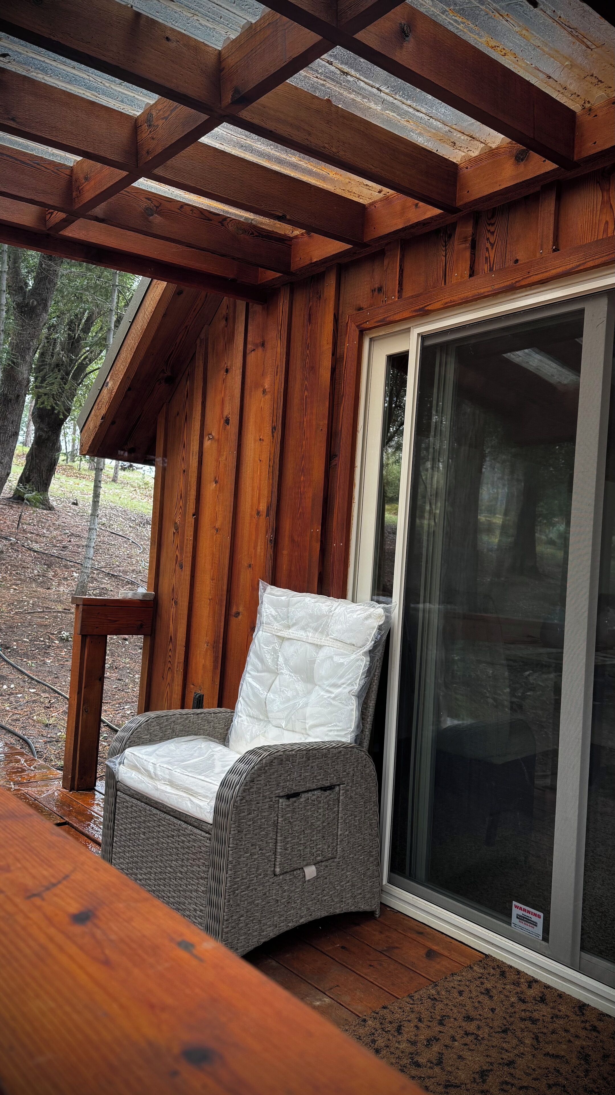 A covered outdoor seating area with a wicker chair, wooden deck, and a sliding glass door.