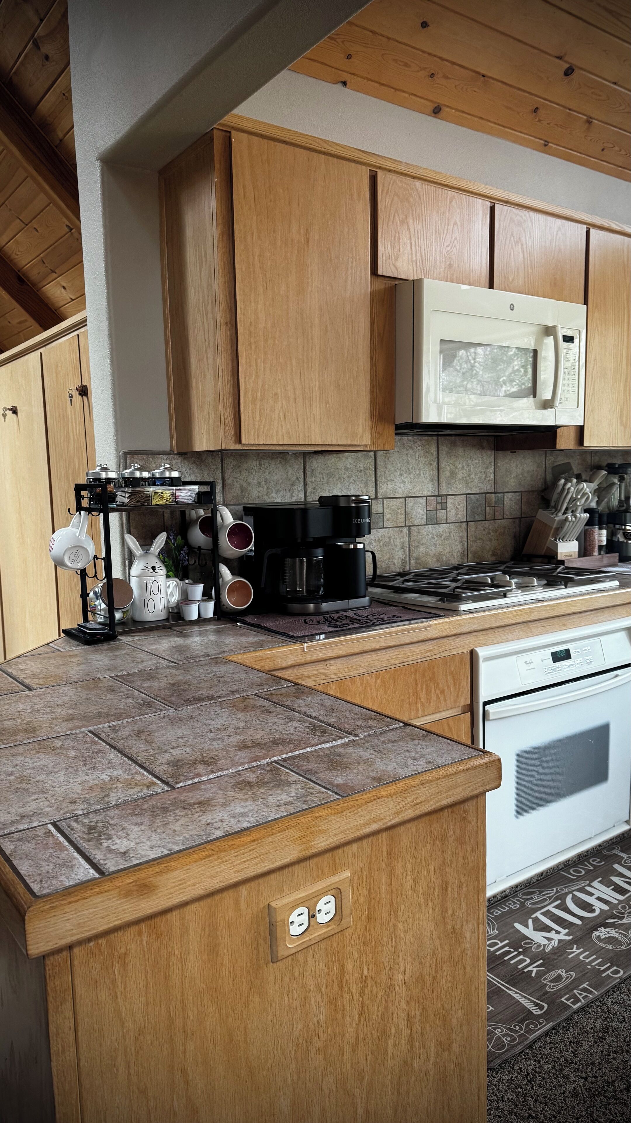 Una cocina con armarios de madera, microondas, cafetera y estufa.