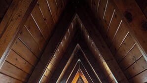 Une chambre située dans un espace de type « loft », avec un plafond en pente, des poutres en bois et un puits de lumière.