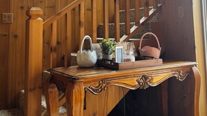 Un escalier en bois, avec une table en bois à sa base, une théière blanche, une plante en pot et un panier.