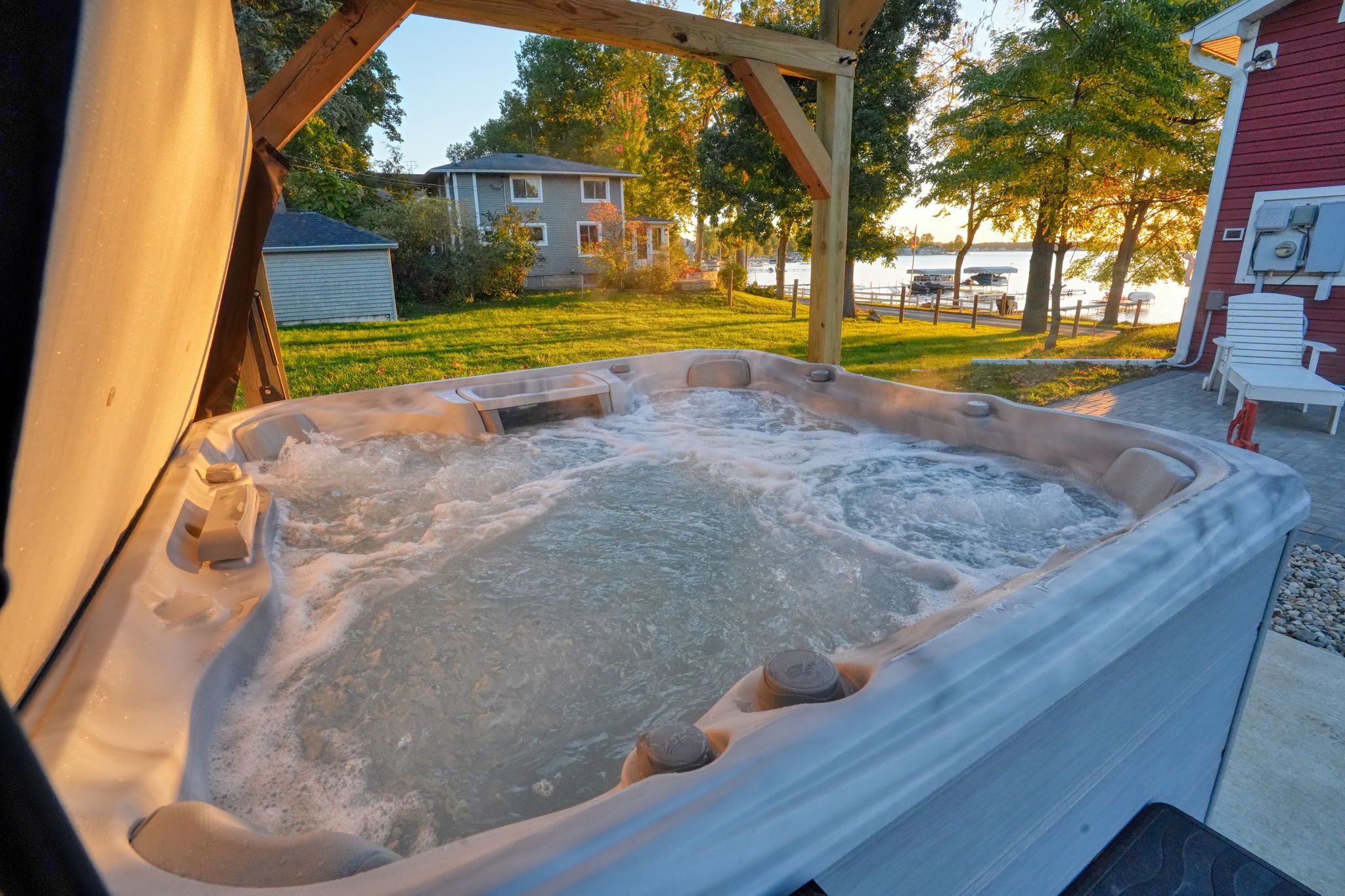 Un bain à remous doté d’une structure en bois au-dessus, entouré d’une pelouse et avec un bâtiment rouge en arrière-plan.