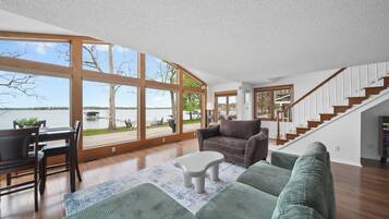 A spacious living room with a large window, a staircase, and a view of a body of water.